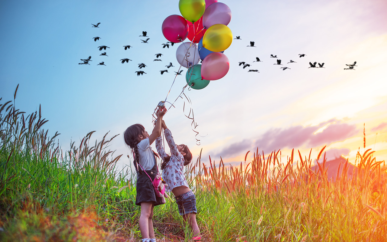 Two children holding onto balloons as the sun rises and birds fly by.