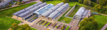 An aerial drone shot of the millennium seed bank, a set of greenhouses and planters, surrounded by green English fields.